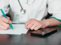 Lekarz pisze zwolnienie, zastanawiając się, na ile lekarz może wystawić L4 jednorazowo. Obok leży telefon.
