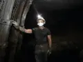 Górnik w kasku z lampką na głowie i masce ochronnej stoi w kopalni. To trudny, ale ważny zawód.