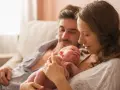 Mama tuli noworodka, tata patrzy z miłością. To piękny obraz opieki na żone po porodzie, pełen czułości i wsparcia.