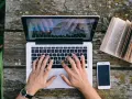 Ręce piszą CV funkcjonalne wzór na laptopie. Obok leży otwarta książka i telefon.