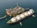 Praca na statku LNG: potężna jednostka z kopułami ładunkowymi przy platformie wydobywczej, holowniki asystują.