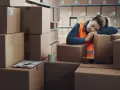 Zmęczona pracownica magazynu śpi na kartonach. Zastanawia się, ile godzin przerwy między zmianami jest jej potrzebne.