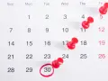 Kalendarz z zaznaczonym 30 dniem miesiąca. Ile godzin pracy to pełny etat w miesiącu? Czerwone pinezki oznaczają ważne daty.