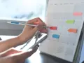 Ręka z ołówkiem zaznacza daty w kalendarzu, planując, ile jest dni pracujących w roku. Kolorowe karteczki pomagają w organizacji.