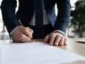 Mężczyzna w garniturze podpisuje dokument. Zbliża się koniec jego okresu wypowiedzenia.
