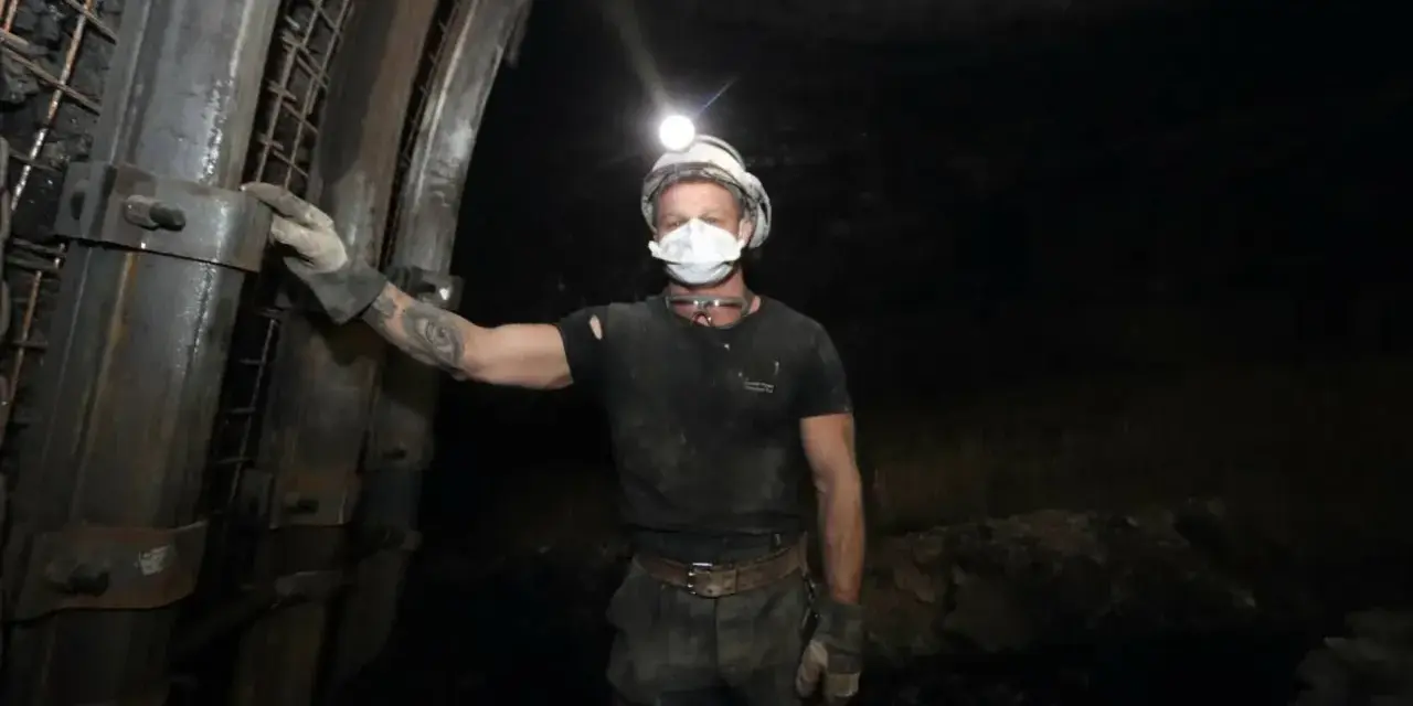 Górnik w kasku z lampką na głowie i masce ochronnej stoi w kopalni. To trudny, ale ważny zawód.