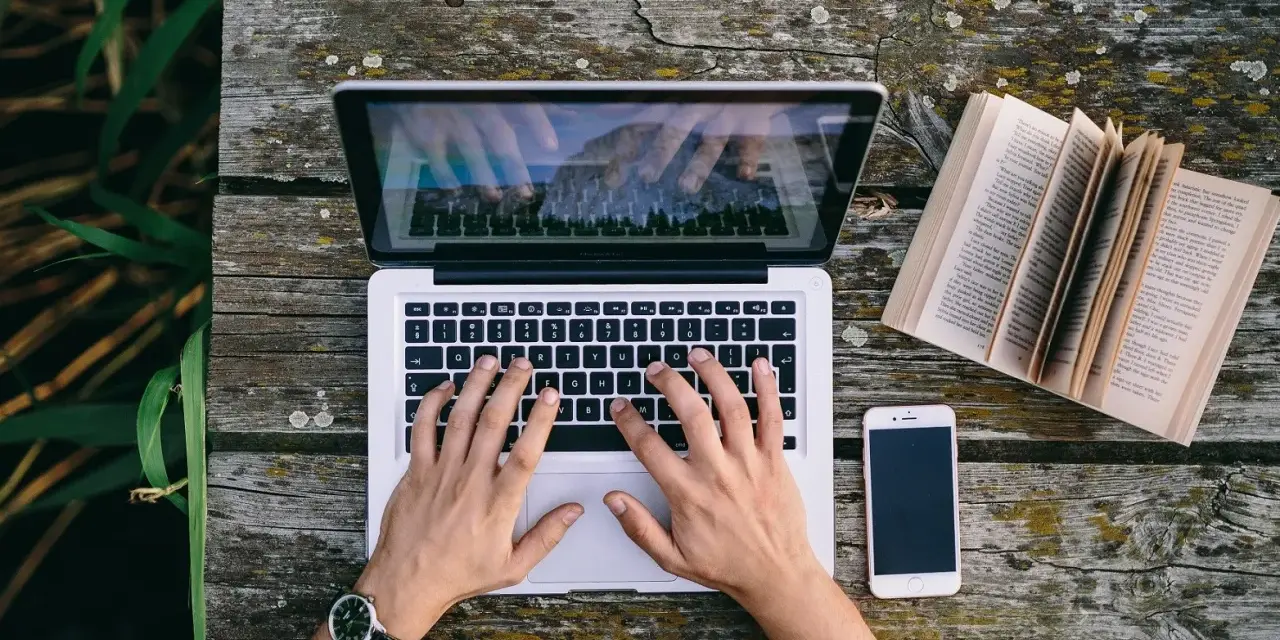 Ręce piszą CV funkcjonalne wzór na laptopie. Obok leży otwarta książka i telefon.