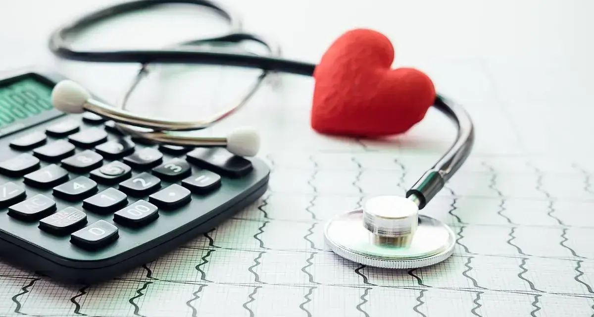 Kalkulator, stetoskop i czerwone serce na tle EKG. Obrazek sugeruje, ile wynosi dobrowolne ubezpieczenie chorobowe.
