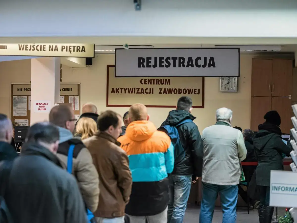 Ludzie stoją w kolejce do rejestracji w centrum aktywizacji zawodowej. Zastanawiają się, czy zasiłek dla bezrobotnych wlicza się do lat pracy.