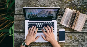 Ręce piszą CV funkcjonalne wzór na laptopie. Obok leży otwarta książka i telefon.