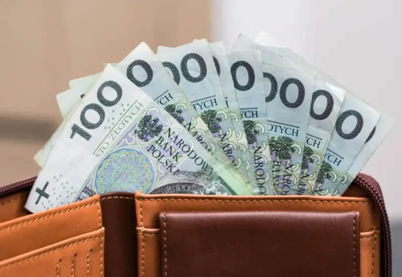 Portfel z banknotami 100 zł. Czy urlop wychowawczy jest płatny? To pytanie nurtuje wielu rodziców, a pieniądze w portfelu mogą pomóc w podjęciu decyzji.