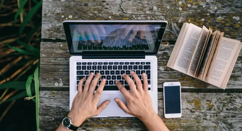 Ręce piszą CV funkcjonalne wzór na laptopie. Obok leży otwarta książka i telefon.